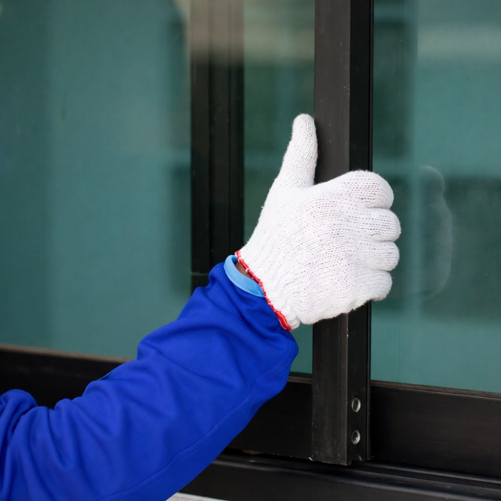 Installer in gloves adjusting a black-framed glass panel during a professional upgrade for replacement windows in Riverside, CA.